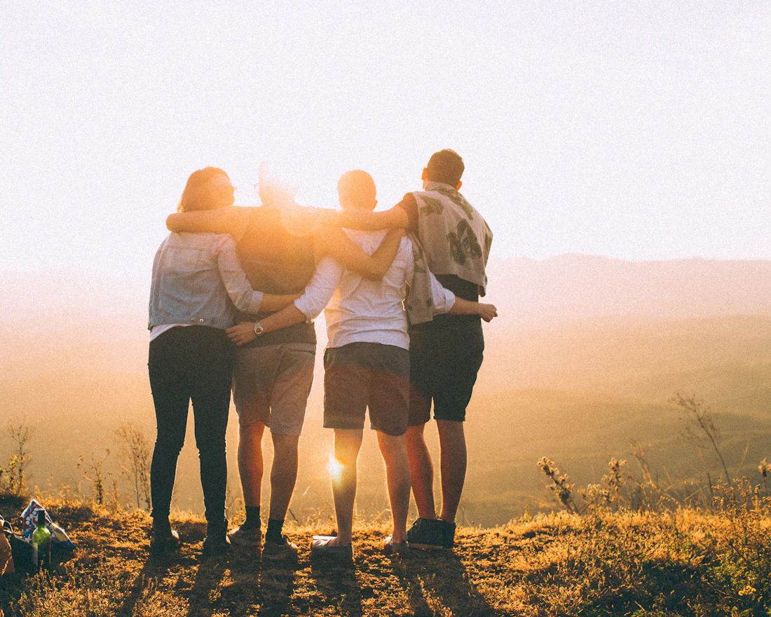 Friends with their arms around each other at sunset